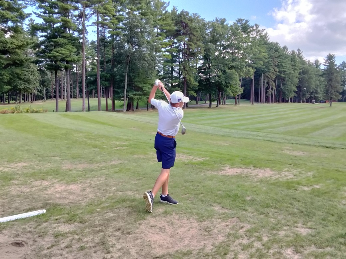 A single golfer posed after hitting the golf ball on a golf course with trees in the background