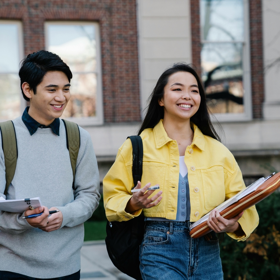 Two young asian students have a conversation walking out of school.